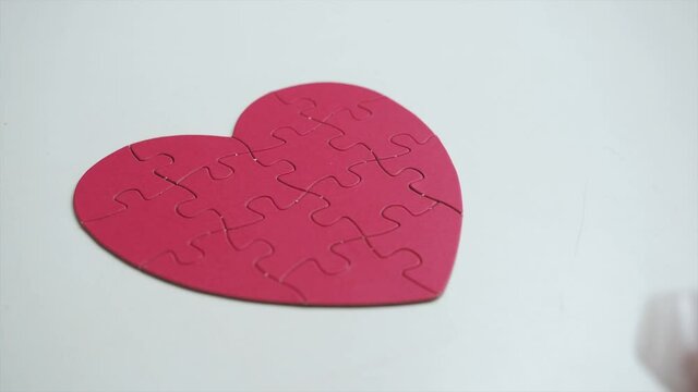 Extreme close up. Top view of woman's hands in white latex medical gloves are putten red heart shaped jigsaw from paper blocks puzzle to white table background