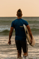Surfer z deską surfingową na tle oceanu, mężczyzna uprawiający zdrowe sporty wodne.