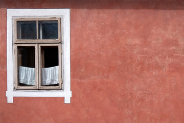 Window on an empty red wall of an old house, cute white curtains in the window