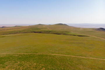 Fototapeta premium Endless steppe in the valley at the foot of the mountains, bathed in bright sunlight. Amazing view on green mountains. mountain, covered with green trees, under a blue sky with clouds.