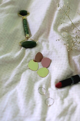 Fashionable earrings, rings, lipstick, face roller and gypsophila flower on beige textile background. Selective focus.