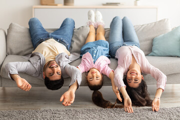 Upside down portrait of happy young family lying on sofa with heads down. Mother, father and...