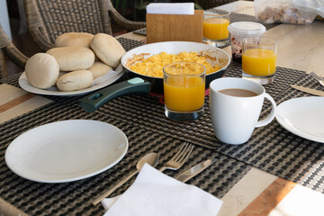 Family breakfast table set with coffee cups, orange juice, scrambled eggs on pan and Chilean country bread