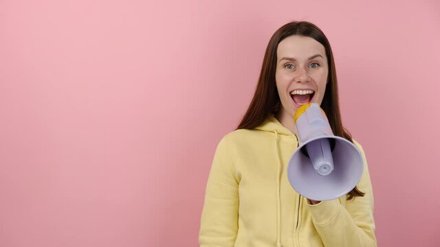 Surprised young female screaming in megaphone showing big hashtag sign, wears yellow hoodie, isolated on pink color background. Marketing network, SMM business, customer attraction campaign concept