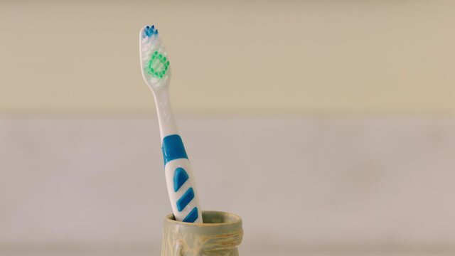 A Toothbrush Being Placed Next To Another In A Cup On Bathroom Counter