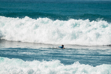 Surfer z deską w wodzie, czekający na nadchodzącą fale, mężczyzna uprawiający sport wodny.