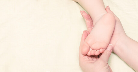 Women's hands hold the foot of a small child close-up, a banner with a place for text. It can be used for children's care cosmetics, skin cream, child body care. copy space