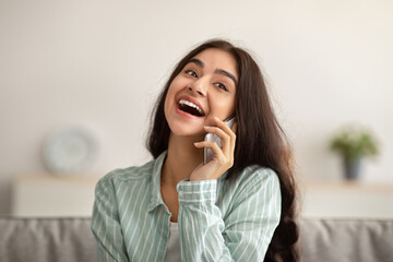 Portrait of happy Indian woman speaking on mobile phone, having conversation with her friend at home