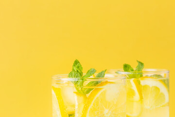 Fresh carbonated lemonade with lemon and mint leaf in a glass on yellow background. Refreshing mineral water with citrus. Bright cheerful summer drink. Close-up, copy space.