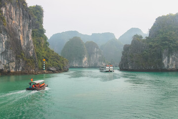 Fototapeta na wymiar Tour boats with tourists cruise the idyllic, turquoise sea and lush, green tropical limestone karst formations at Ha Long Bay, Vietnam.