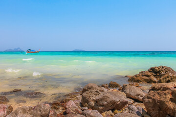 Idyllic tropical blue, turquoise aqua marine water at Loh Moo Dee Beach with a Thai Long-tail boat on the horizon at Koh Phi Phi, Thailand.