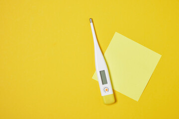 electronic thermometer on yellow background copy space top view