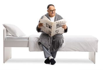 Mature man in a robe relaxing on a bed with a newspaper