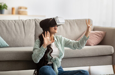 Millennial Indian woman in virtual reality glasses exploring cyberspace, playing interactive video game indoors