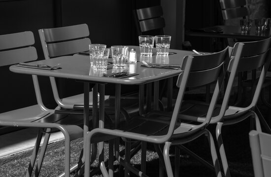 Empty Cafe Terrace Setting For Lunch. Nobody. Abandoned Lifestyle Background. Impossible Dinner Party, Socializing Limits Metaphor, Economic Crisis Concepts. Black White Toned Photo.