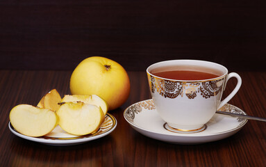 Cup of tea and plate with apples on dark background
