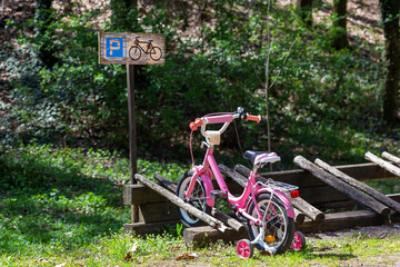 A small, pink children's bicycle is parked in a designated area with a parking sign.