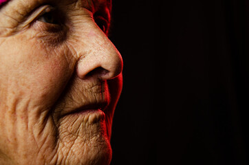 Old grandmother's face close up. Close-up of wrinkled old face. A portrait photo of an old grandmother. An old face in the dark. Aged skin on the face. Seniors concept