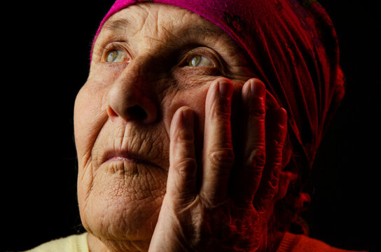 The face of an old grandmother close up. Portrait photo of a grandmother on a dark background. Old grandmother in the dark close-up. Grandmother's wrinkled face close-up.