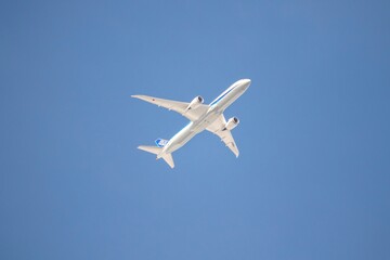 A close portrait of a touristic airliner plane flying low through a blue cloudless sky. It is a white airplane with a blue stripe on it.