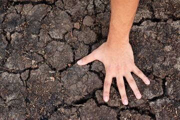 Human hand on dry black soil with cracks. Denotes water scarcity or drought 