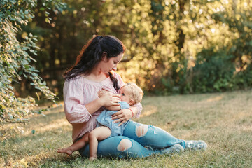 Young Caucasian mother breastfeeding daughter baby in park outdoor. Health of little kids children. Toddler girl sucking milk from mom breast. Bonding and attachment with child kid.