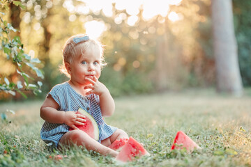 Summer picnic food. Cute Caucasian baby girl eating ripe red watermelon in park. Funny child kid...