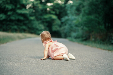  Cute baby girl crawling on road in park outdoor. Adorable child toddler exploring studying the world around. Healthy physical development. View from back behind. Authentic lifestyle happy childhood.