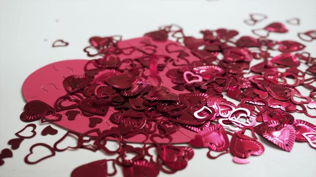 Many shiny sparkling hearts falling on big red puzzle shaped jigsaw on white table background. Celebrate Valentines day