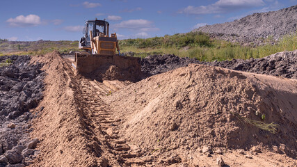 a bulldozer moves sand while building a dirt road to a new construction site