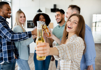 Group of multiracial friends toasting with beer bottles, saying CHEERS, celebrating something, having party at home