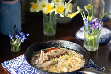 Stew of chicken, lentil, lemon, spices in pan on blue textile cover on brown wooden table and flowers in vases
