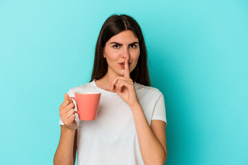 Young caucasian woman holding a mug isolated on blue background keeping a secret or asking for silence.