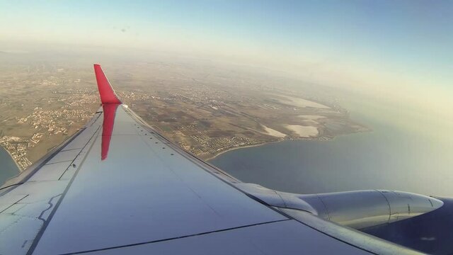 View of the wing and engine of the aircraft from the window. The plane has just taken off and is making a turn over the island of Cyprus.
