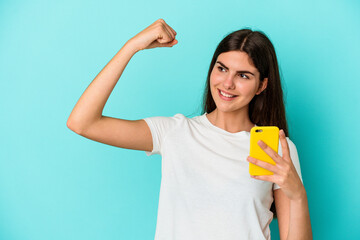 Young caucasian woman holding a mobile phone isolated on blue background raising fist after a victory, winner concept.