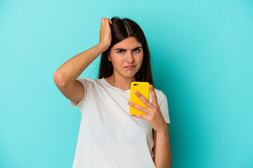 Young caucasian woman holding a mobile phone isolated on blue background being shocked, she has remembered important meeting.