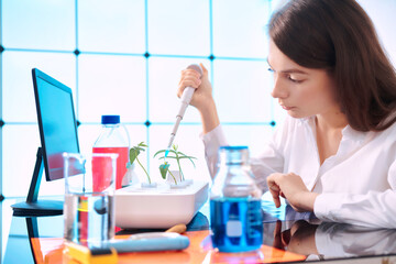 Young woman with a pipette in a plant laboratory. Study of the effect of fertilizers and growth...