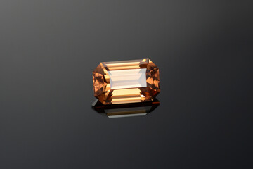 Natural mined yellowish brown cognac color emerald cut flawless transparent zircon loose gemstone setting for making jewelry on dark gray gradient background. Reflection on black glass surface.