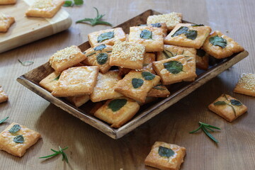 Homemade crackers decorated with herb leaves, sesame seeds, poppy seeds and salt