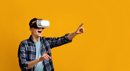 Naklejka premium Cool young guy in virtual reality headset controlling cyber environment, pushing invisible button on virtual screen