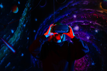 Emotional happy girl in modern virtual reality glasses with neon red and blue light on the background of space in the playroom. VR headset concept