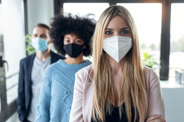 Multiethnic business team wearing a hygienic face mask while looking at camera in the coworking...