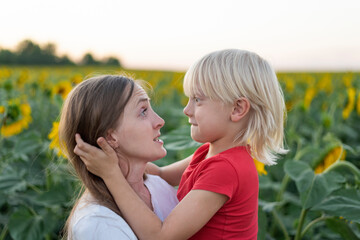 Fototapeta premium Mom and son make each other's faces. Cheerful portrait of mother and son on sunflower field background.