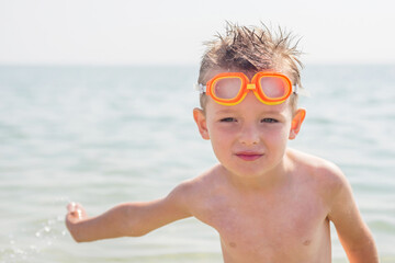 Portrait of a cheerful boy in goggles for swimming while relaxing on the sea. Summer vacation