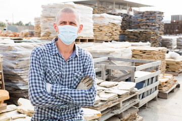 Portrait of man worker in face mask standing in warehouse of hardware store