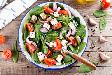 Fresh vegetables salad from spinach, tomato, feta cheese, onion in plate on a wooden table. Top view
