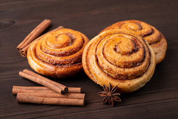 Fresh baked cinnamon rolls on brown table. Cinnamon sticks and anise star as decoration on the picture.
