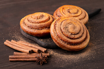 Baking composition: homemade bun on cutting board, anise star and cinnamon sticks near them. Sweet food on the braun table, close up.