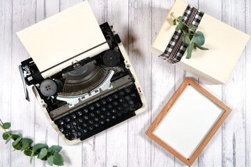 Vintage typewriter. On-trend farmhouse theme flatlay craft product mockup with farmhouse style decor, stack of books, and bow on a white wood background. Negative copy space for your design here.