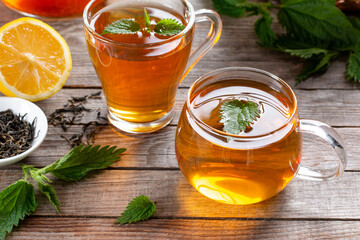 A cup of nettle tea on a table, with fresh stinging nettles in the background